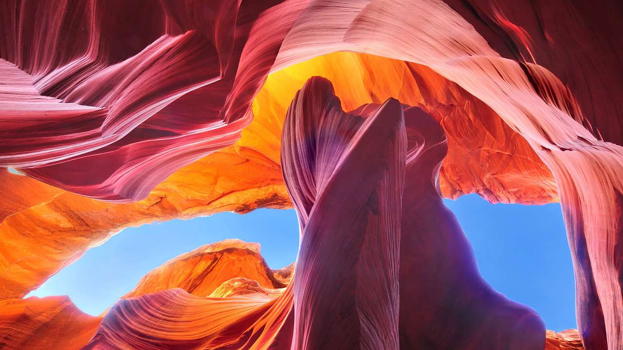 A colorful pink and orange rock formation with blue sky seen through gaps