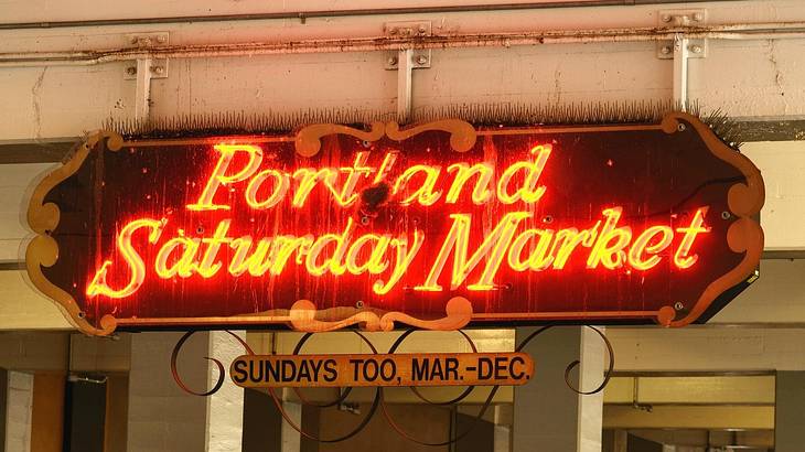 A black sign with illuminated red-yellow text saying "Portland Saturday Market"