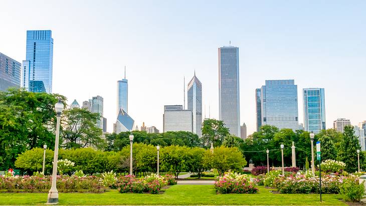 A green park with lampposts and high rise buildings in the background