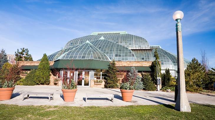 A building with a glass roof with grass, trees and plants, and a lamp in front A building with a glass roof with grass, trees and plants, and a lamp in front
