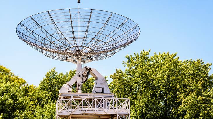 A big radio telescope standing in front of green trees