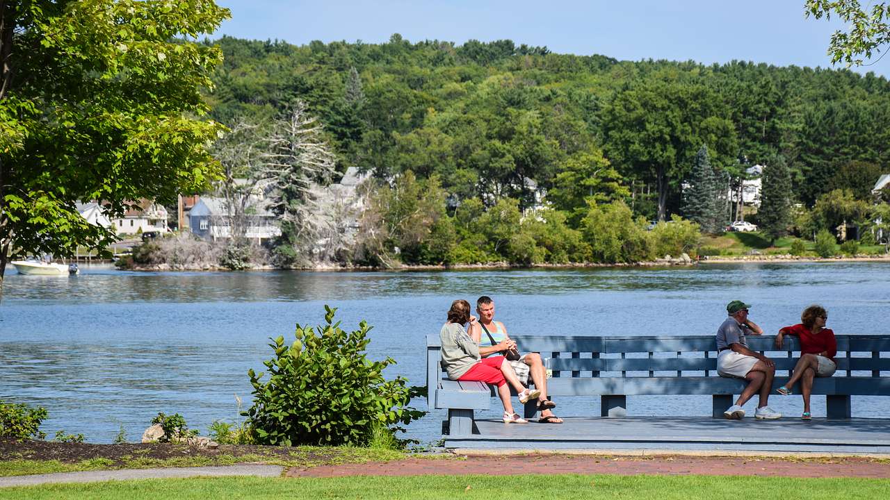 Two people sitting on a bench with a body of water and a hill behind them