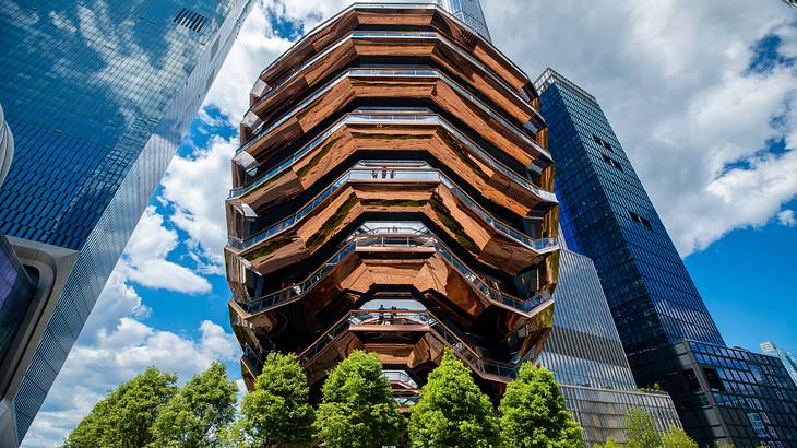 A large bronze structure with skyscrapers surrounding it and trees below