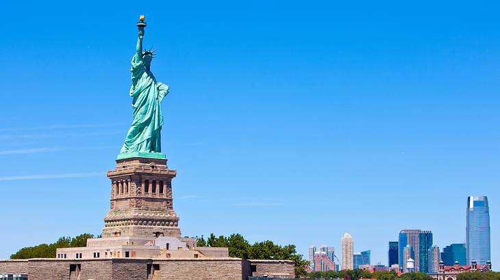 The Statue of Liberty under a blue sky, with buildings in the distance