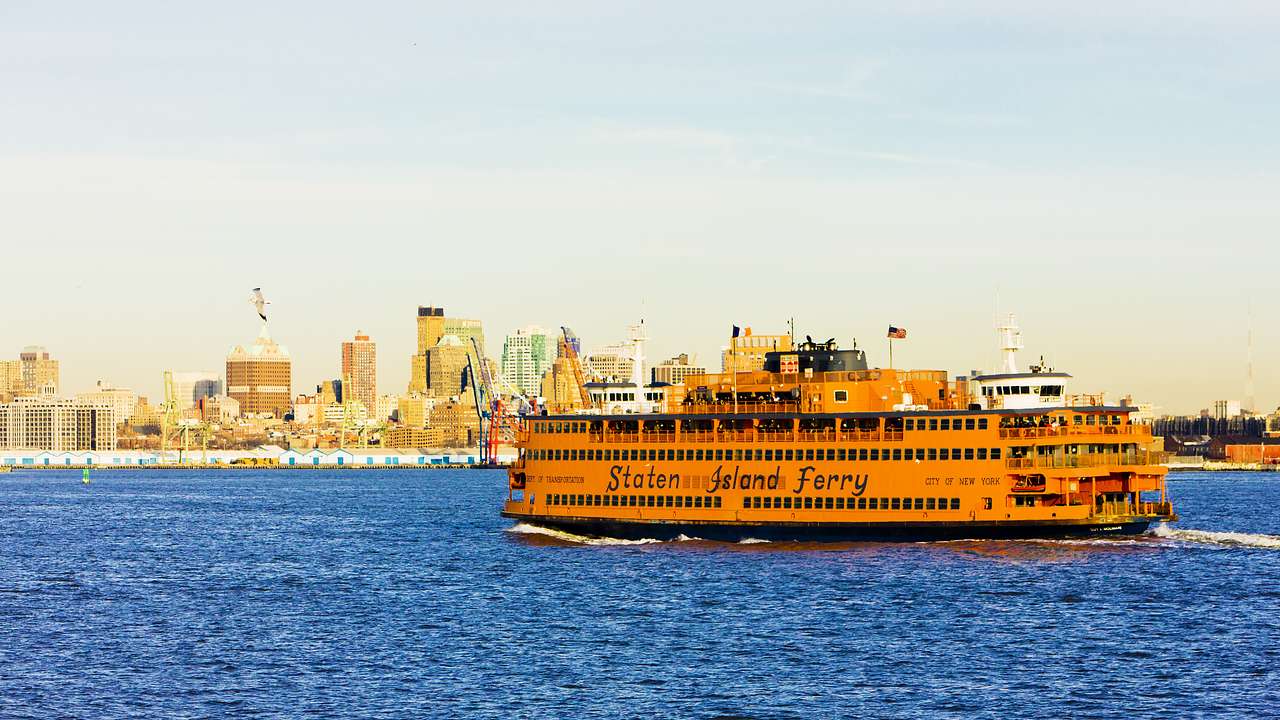 A yellow passenger ferry on the water with a city skyline behind it