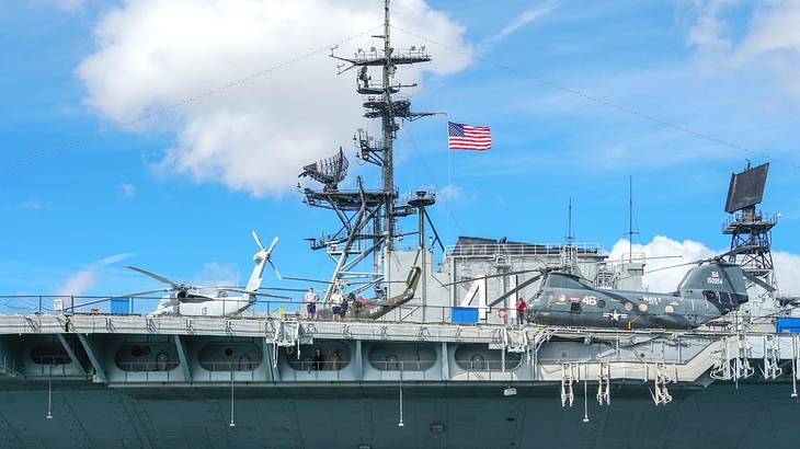 A military ship with a US flag under a blue sky with some clouds