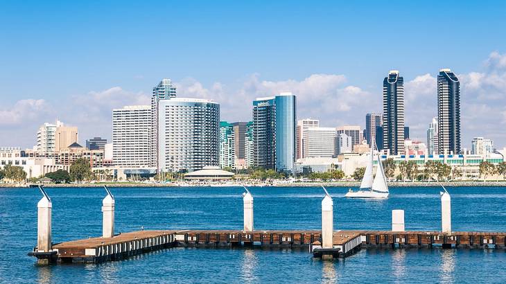 A bay with a boat dock and a sailboat on the water in front of city buildings A bay with a boat dock and a sailboat on the water in front of city buildings