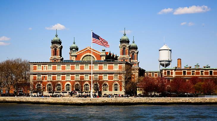 A red brick building under blue sky with an American flag and water in front