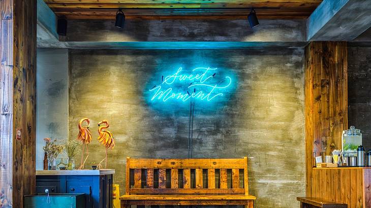 A bench in front of a wall with a blue neon sign that says "Sweet Moment"