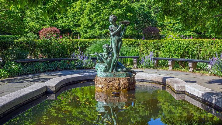 A pond with a statue and greenery surrounding it A pond with a statue and greenery surrounding it