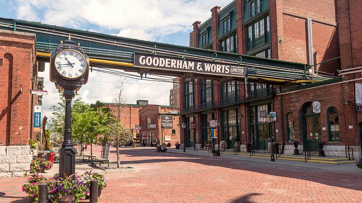 Old red brick buildings and courtyard with a sign, facing a clock pillar in Toronto