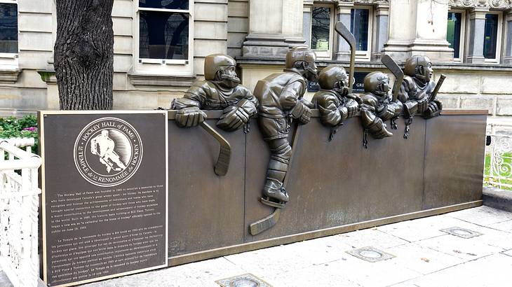 A row of human sculptures next to a plaque outside the Hockey Hall of Fame in Toronto