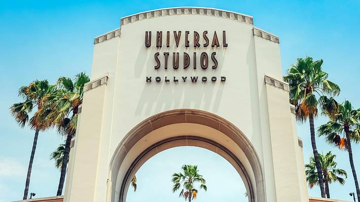 A white arch with a "Universal Studios Hollywood" sign and palm trees next to it