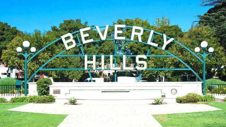 A sign that says "Beverly Hills" in a garden with green grass and trees