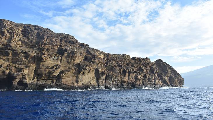 A large cliff surrounded by ocean under a blue sky