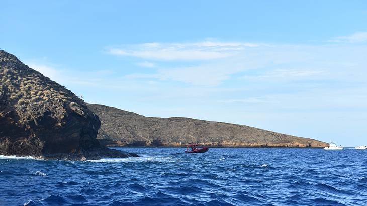 A red boat on the ocean with rocks to the side under blue sky A red boat on the ocean with rocks to the side under blue sky