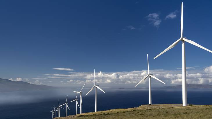 White wind turbines atop a mountain, with the sky and mountains in the background White wind turbines atop a mountain, with the sky and mountains in the background