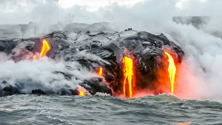 Molten lava and steam coming out of a hilly volcano into the surrounding ocean