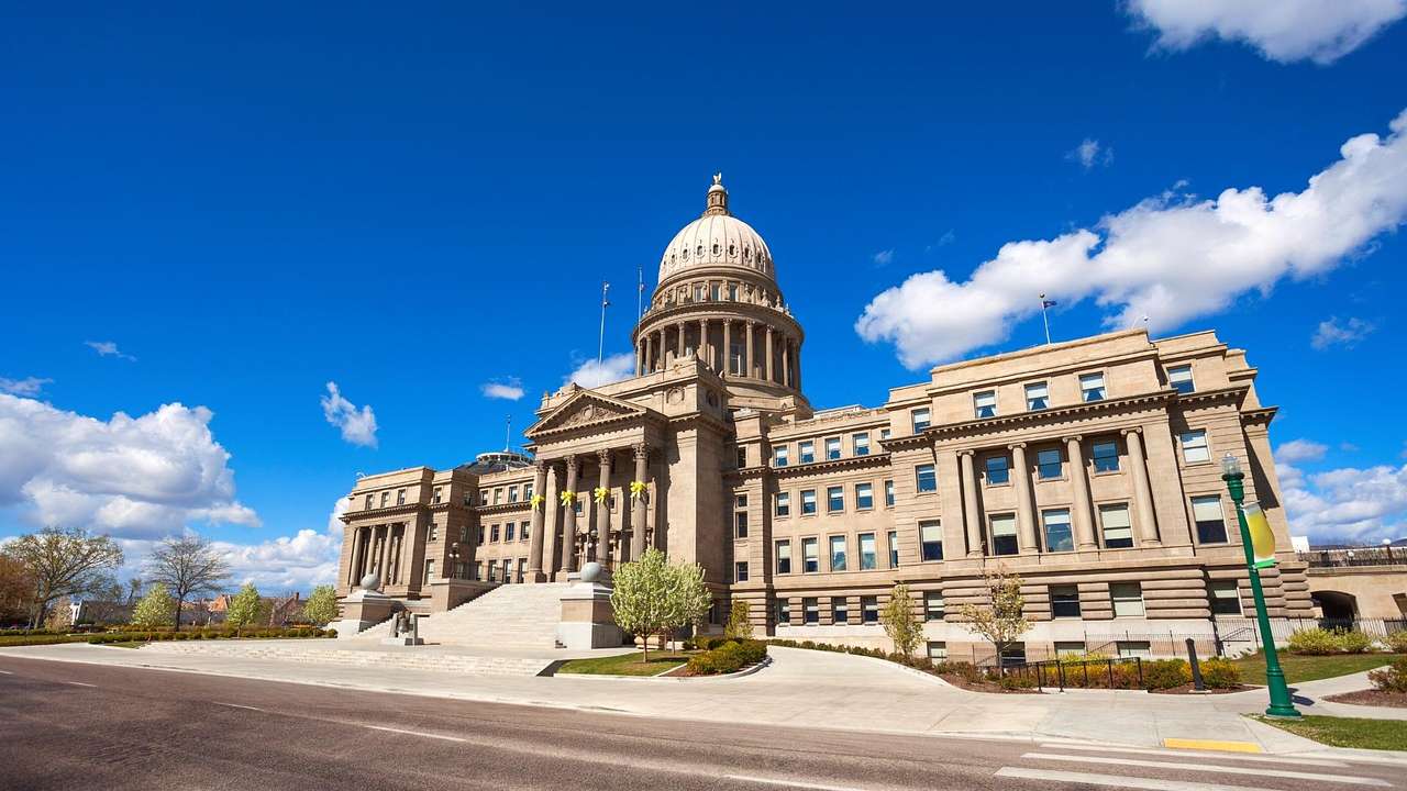 A neoclassical capitol building with a dome facing a road on a nice day