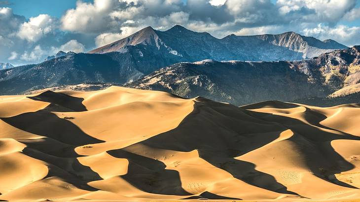 Sand dunes against rugged mountains under a cloudy sky