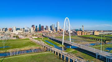 A city skyline next to grass and a white arch under a blue sky