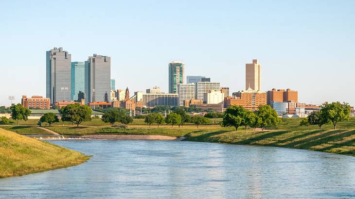 A city skyline next to grass and water under a blue sky