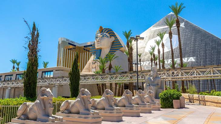 A sphinx statue and a mirrored pyramid with statues and palm trees in front