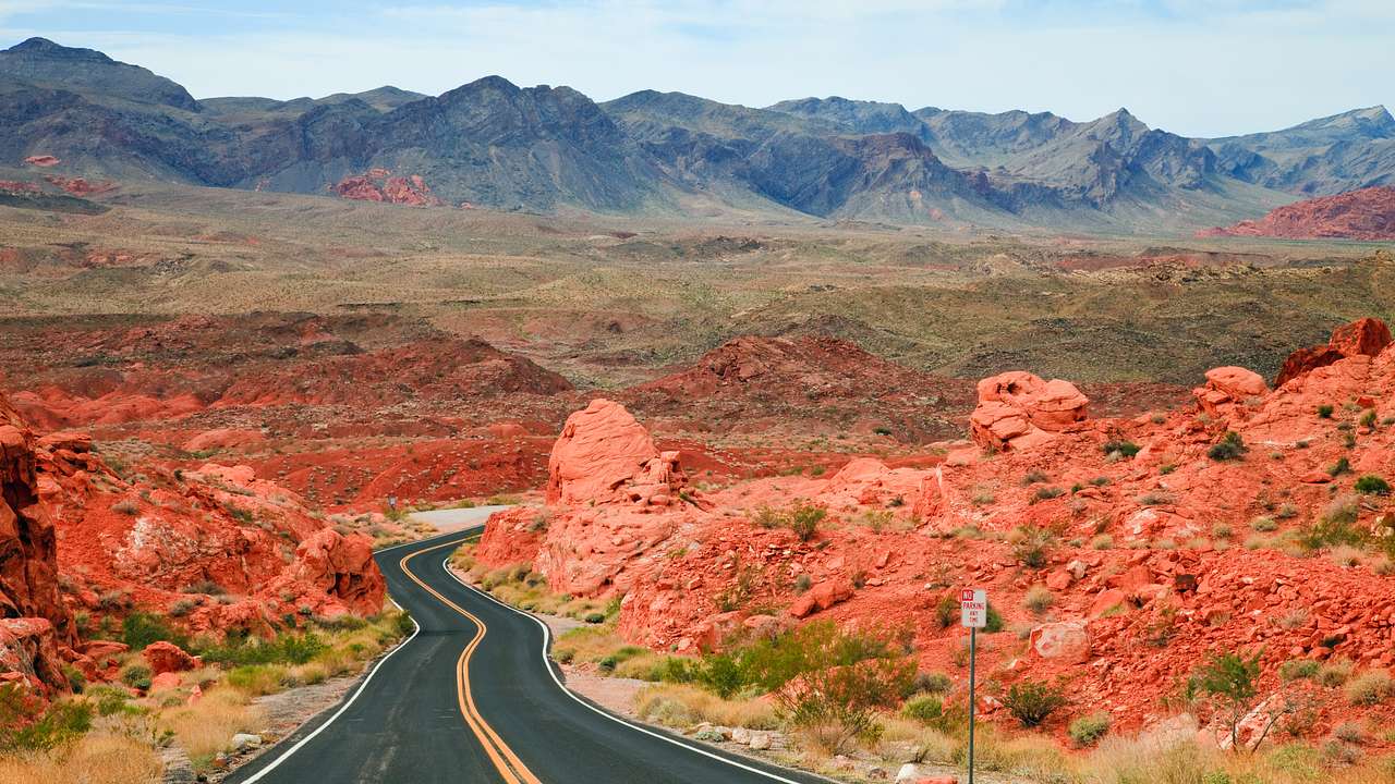 A road winding through red rocks with a mountain range in the distance