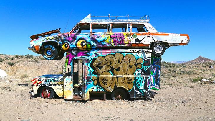 An old car on top of an old bus covered with graffiti in the desert