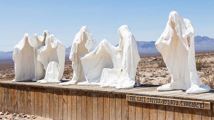 Ghost like statues on a wooden podium in the desert
