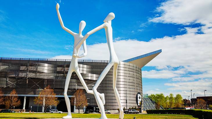 Two white statues on the grass in front of a metallic building