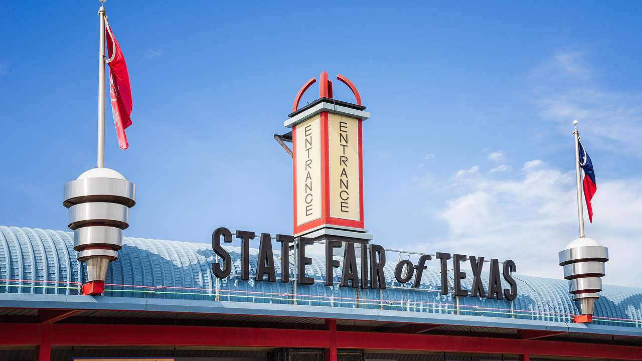 The entrance to a fair with a "State Fair of Texas" sign and red flags