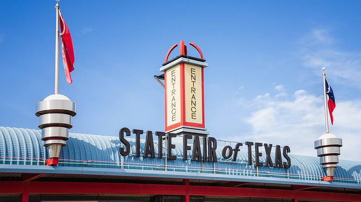 The entrance to a fair with a "State Fair of Texas" sign and red flags