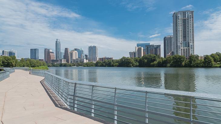 A path running alongside a river with skyscrapers on the other side