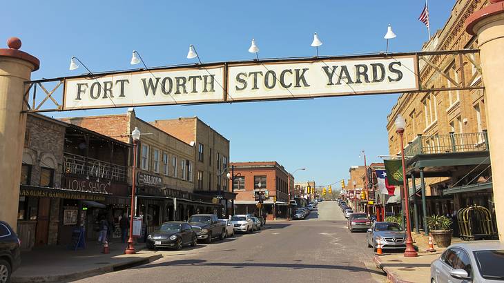 A sign that says "Fort Worth Stockyards" over a street with cars and buildings