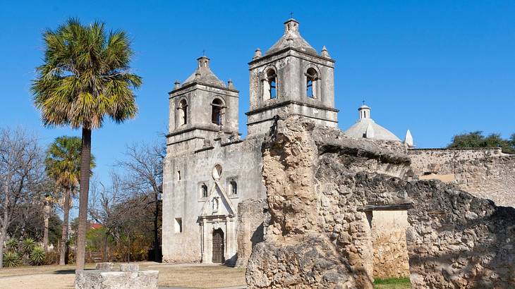 An old-fashioned mission with two towers and palm trees next to it