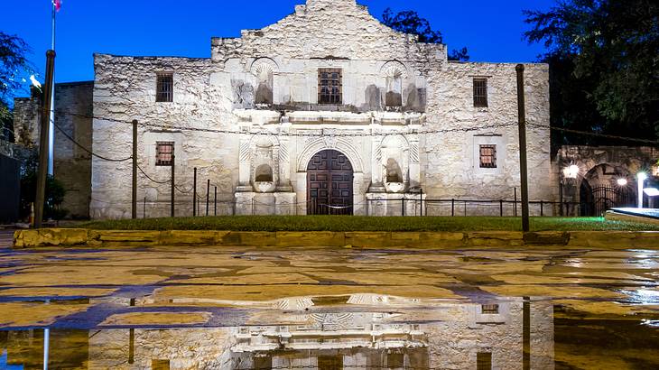 An old fashioned building at night with puddles with reflections in them in front