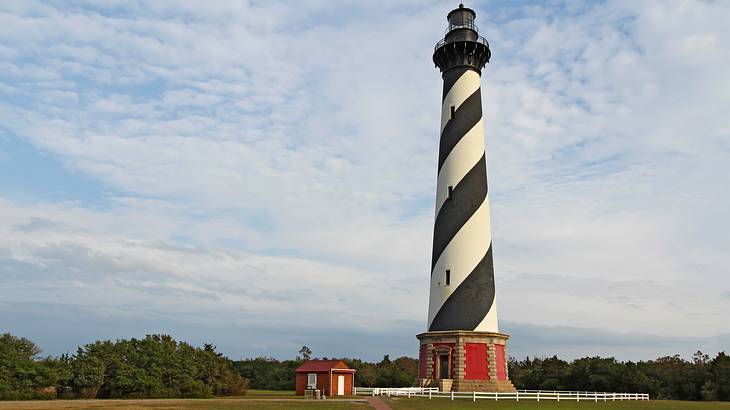 A black and white lighthouse standing on the grass with a red hut beside it A black and white lighthouse standing on the grass with a red hut beside it