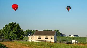 Two hot air balloons flying above a field with a small building in it