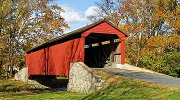 A red covered bridge next to grass and autumn trees