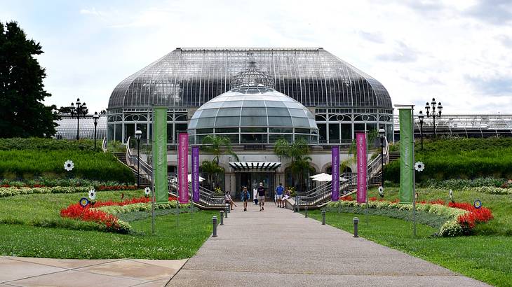 A glass conservatory building next to a path, grass, and flowers