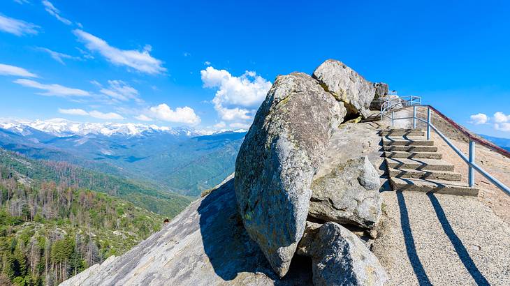 A granite rock hill with stairs carved into it under a blue sky with clouds