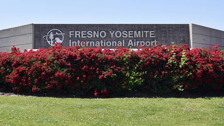 A "Fresno Yosemite International Airport" sign next to grass and red flowers