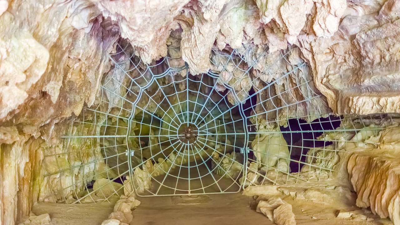 A gate shaped like a spider web at the entrance to a cave