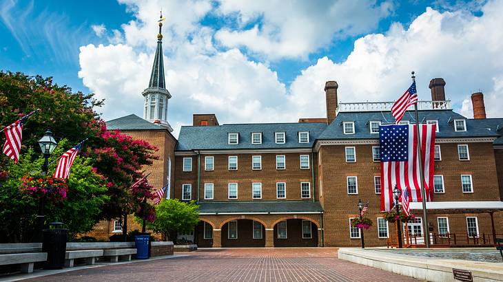 A red brick building with a steeple, many windows, and a large US flag on it