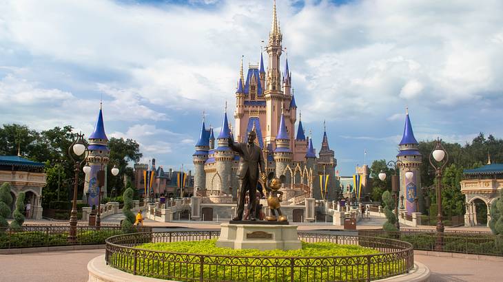 A pink castle with a statue of a man and a mouse character in front