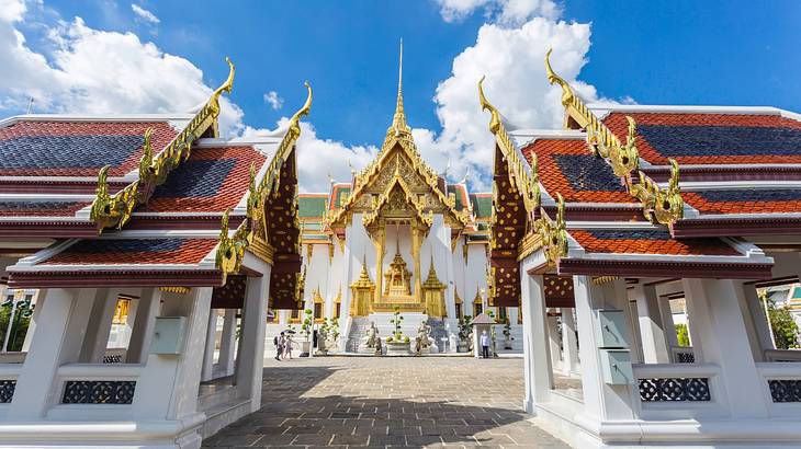 The exterior of a stunning Buddhist temple with gold details on a partly cloudy day