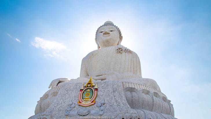 A large white marble Buddha statue against a blue sky from below