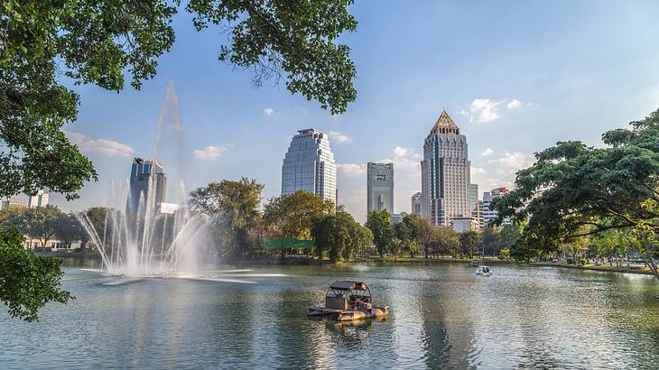A lake with a fountain surrounded by trees and skyscraper buildings in the background
