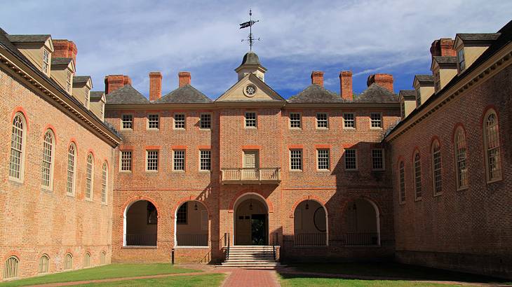 A large brick building with a wind vane on top and a lawn in front